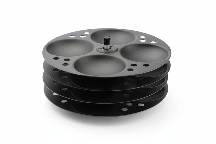 A black non-stick idli stand with four racks, made of stainless steel, designed for making idlis.