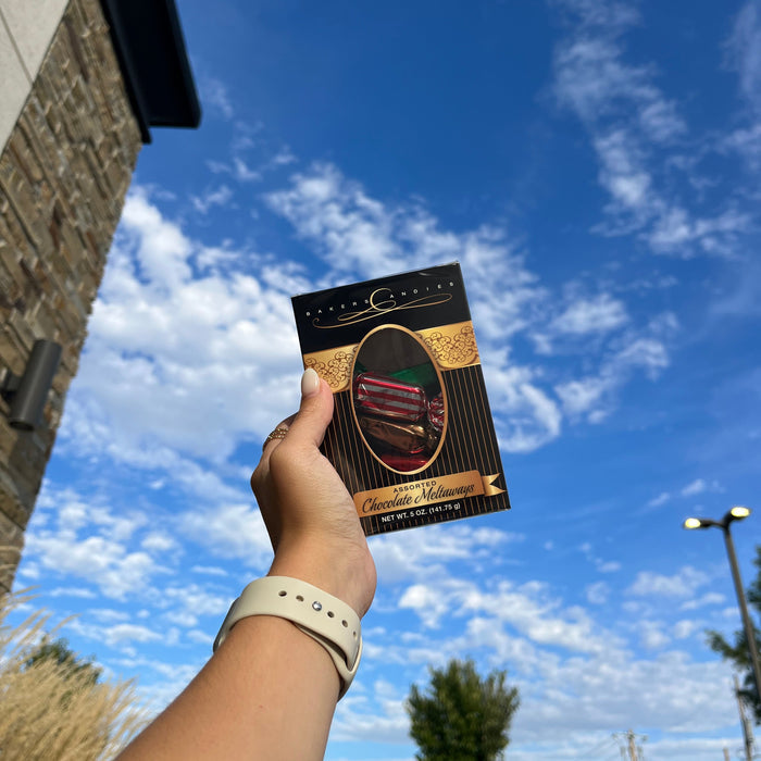 Bakers Candies 5oz Chocolate Meltaways Window Box Being held by a person in front of a sky background.