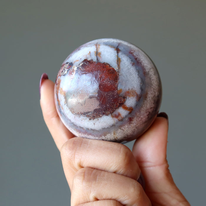 fingers holding Blue Red Chalcedony Sphere