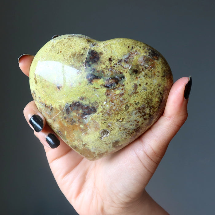 Heart-shaped green Opal stone held in a hand against a dark background